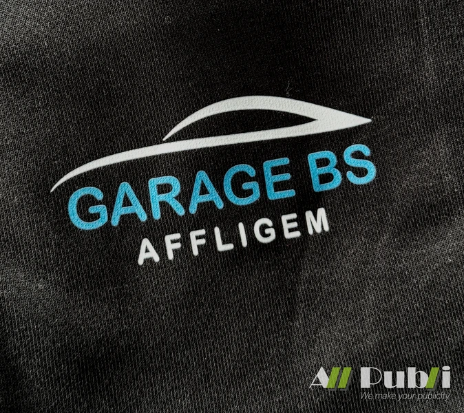 Detail van het blauwe en witte Garage BS Affligem-logo op zwart textiel
