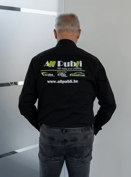 Achterzijde van een zwart overhemd met het All Publi-logo en websiteadres